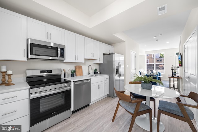 kitchen with white cabinets, appliances with stainless steel finishes, light hardwood / wood-style flooring, and sink