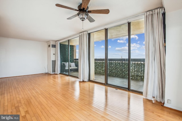 unfurnished room with light wood-type flooring, a wall of windows, and a ceiling fan