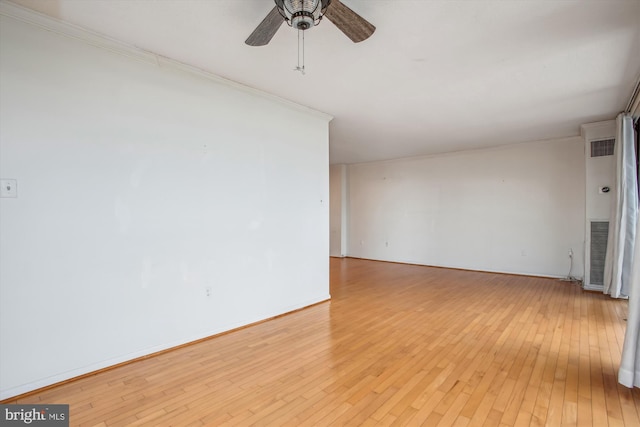 spare room featuring crown molding, light wood finished floors, visible vents, a ceiling fan, and baseboards