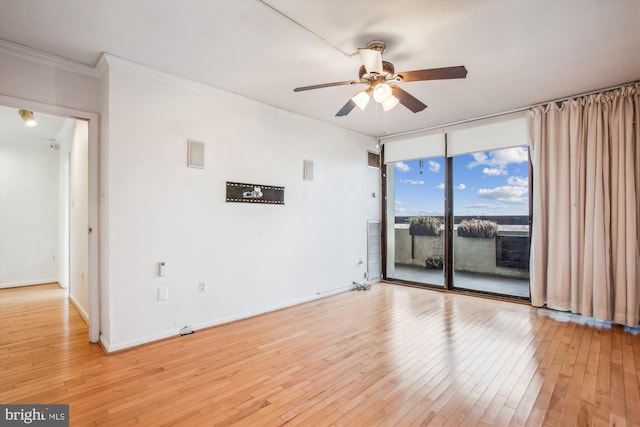 empty room with floor to ceiling windows, crown molding, light wood-style flooring, ceiling fan, and baseboards