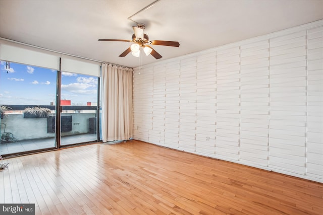 unfurnished room with a wall of windows, light wood finished floors, and a ceiling fan