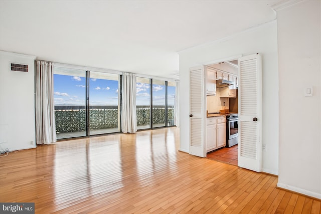 unfurnished living room with visible vents, baseboards, light wood-style flooring, ornamental molding, and a wall of windows