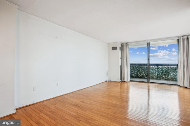 unfurnished room with baseboards, visible vents, light wood-style flooring, expansive windows, and crown molding