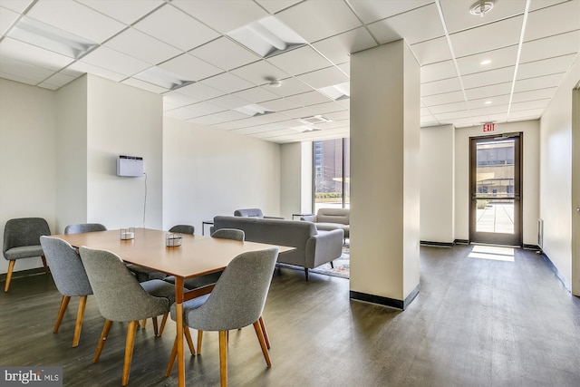 dining room featuring dark wood-style floors, a drop ceiling, and baseboards