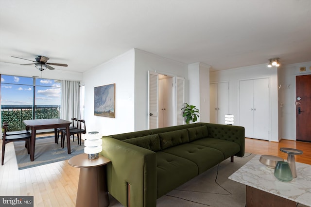 living area with ornamental molding, a wall of windows, ceiling fan, and wood finished floors