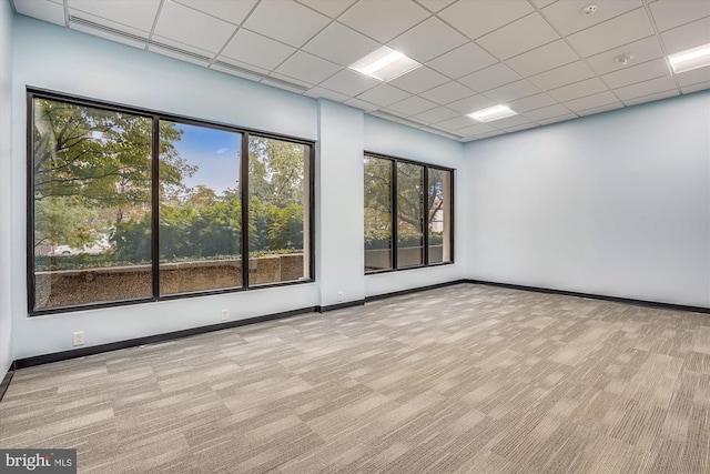 spare room featuring a paneled ceiling, light colored carpet, and baseboards