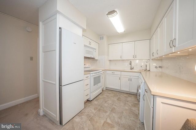 kitchen featuring tasteful backsplash, white appliances, sink, washer / dryer, and white cabinetry