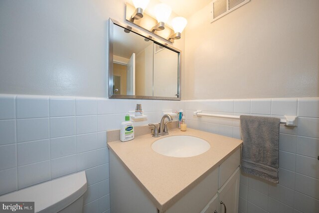 bathroom featuring vanity, tile walls, and toilet