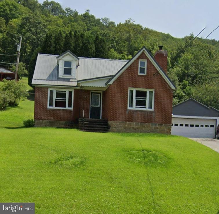 view of front of property with an outbuilding, a wooded view, a detached garage, a front yard, and metal roof