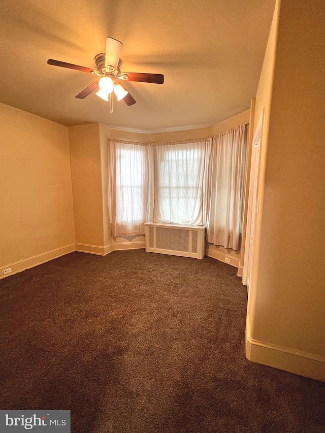 empty room featuring dark colored carpet, radiator heating unit, and ceiling fan