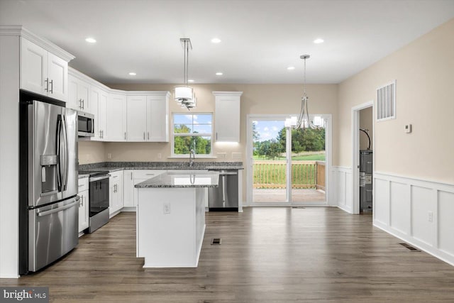 kitchen with decorative light fixtures, stainless steel appliances, white cabinetry, and a kitchen island