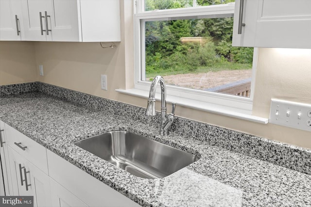 details featuring white cabinets, light stone countertops, and sink