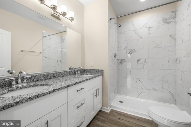 bathroom featuring wood-type flooring, a tile shower, vanity, and toilet