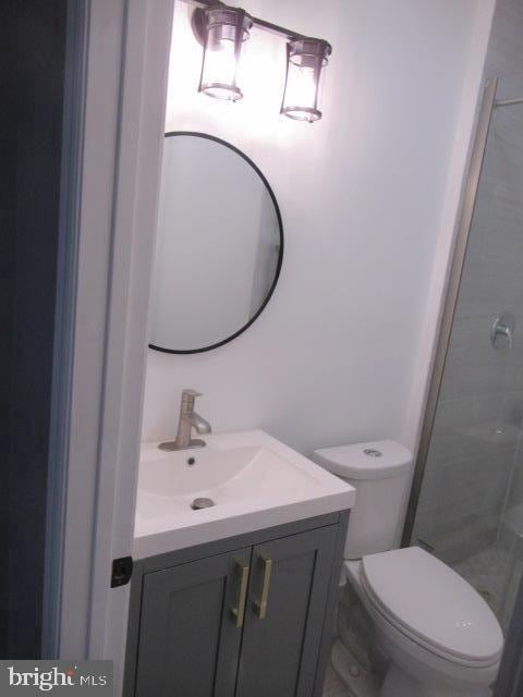 bathroom featuring a tile shower, vanity, and toilet