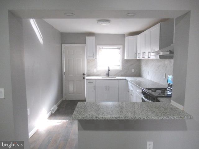 kitchen with kitchen peninsula, sink, range, and white cabinetry