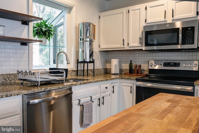 kitchen featuring dark stone countertops, white cabinets, appliances with stainless steel finishes, and backsplash