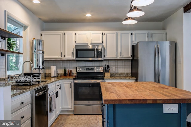 kitchen featuring hanging light fixtures, decorative backsplash, white cabinets, stainless steel appliances, and dark stone counters