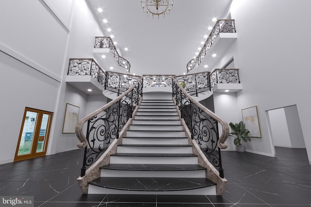 staircase with french doors, a high ceiling, and an inviting chandelier