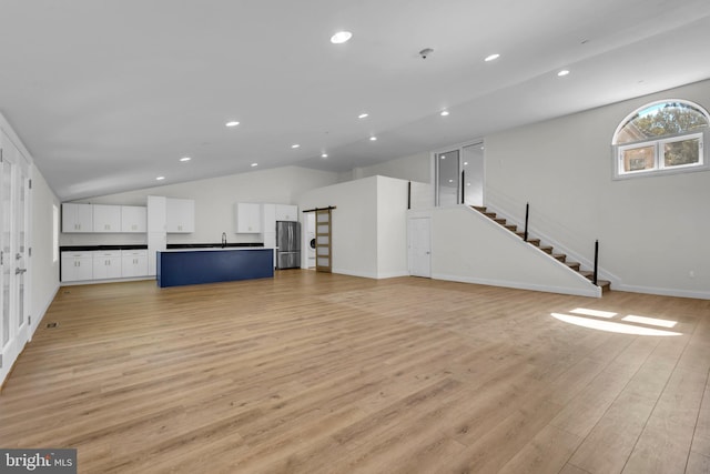 unfurnished living room featuring lofted ceiling, light hardwood / wood-style floors, and sink