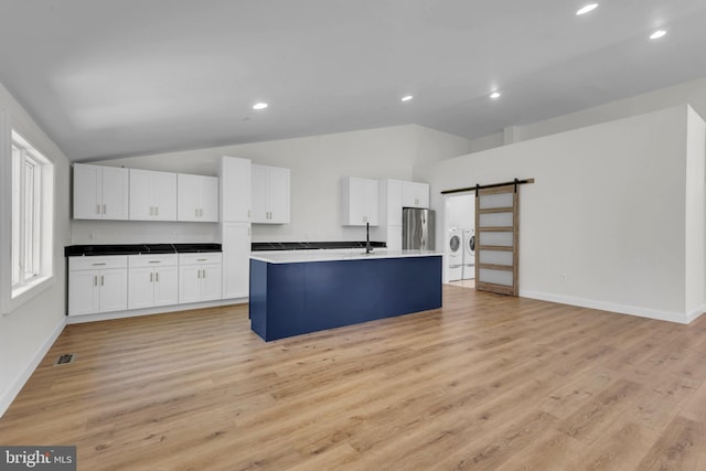 kitchen with stainless steel refrigerator, a barn door, vaulted ceiling, and white cabinets