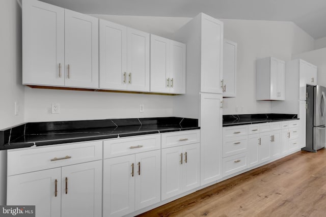 kitchen featuring white cabinets, lofted ceiling, stainless steel fridge, and light hardwood / wood-style flooring