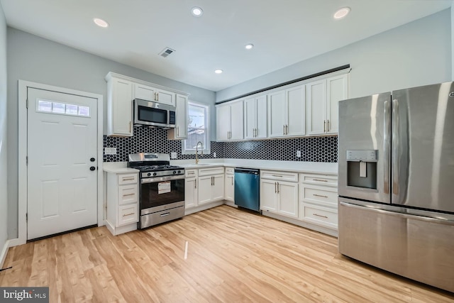 kitchen featuring white cabinets, light hardwood / wood-style floors, appliances with stainless steel finishes, and tasteful backsplash