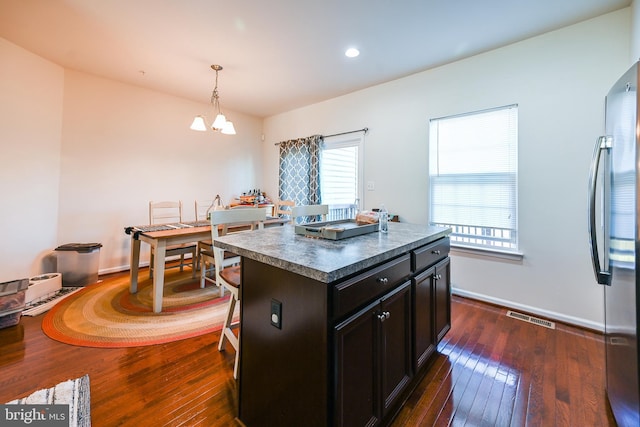 kitchen featuring dark wood-type flooring, a center island, stainless steel fridge, and hanging light fixtures