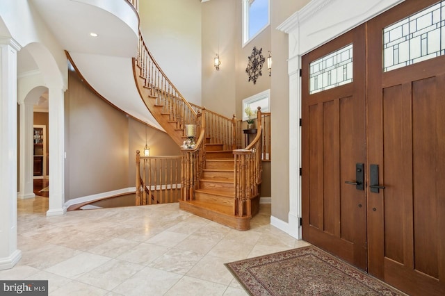 foyer with decorative columns, a towering ceiling, and light tile patterned floors