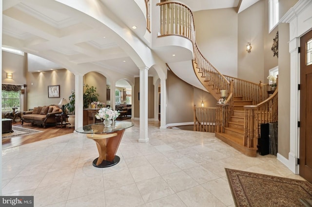 foyer entrance featuring coffered ceiling, light hardwood / wood-style floors, decorative columns, crown molding, and a towering ceiling