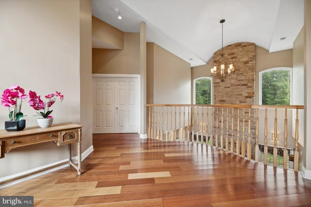 corridor featuring high vaulted ceiling, hardwood / wood-style flooring, an inviting chandelier, and plenty of natural light