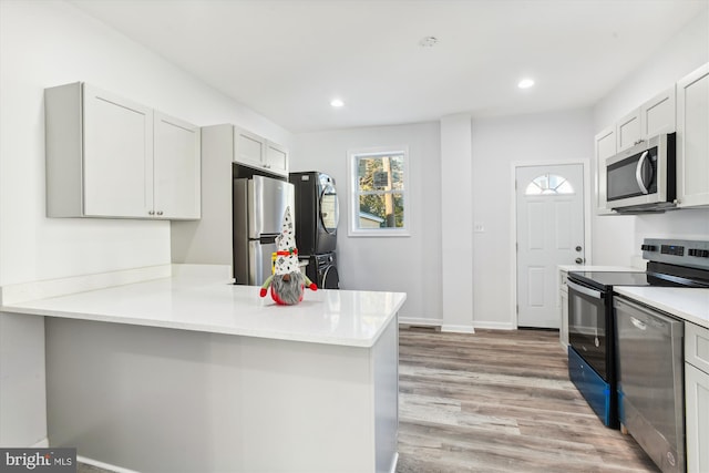 kitchen with kitchen peninsula, stainless steel appliances, light hardwood / wood-style flooring, stacked washer and clothes dryer, and white cabinets