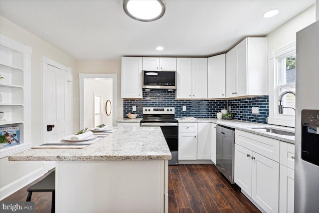 kitchen with white cabinets, appliances with stainless steel finishes, dark hardwood / wood-style floors, and a kitchen island