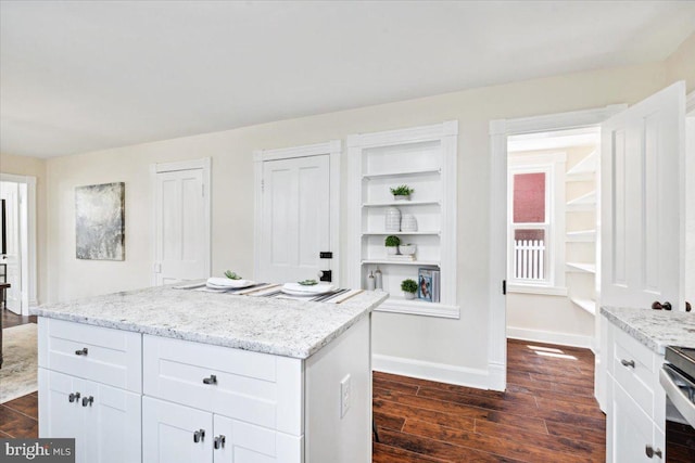 kitchen with white cabinetry, light stone counters, a kitchen island, and dark hardwood / wood-style flooring