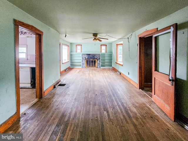 unfurnished living room with ceiling fan, a fireplace, plenty of natural light, and hardwood / wood-style floors