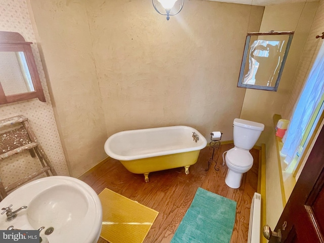 bathroom featuring hardwood / wood-style flooring, toilet, and a tub to relax in