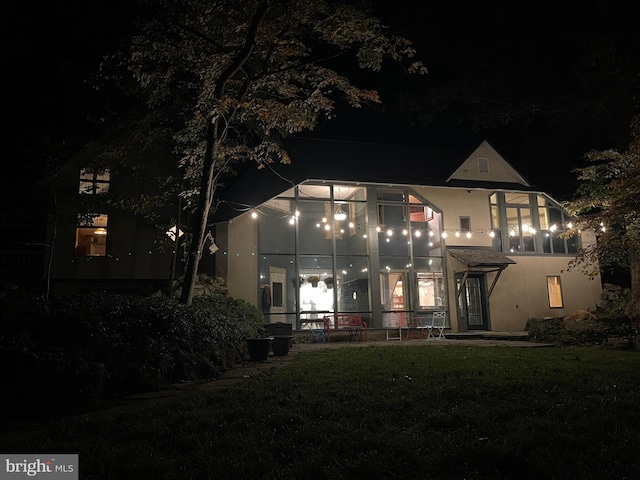 back house at twilight with a sunroom and a lawn