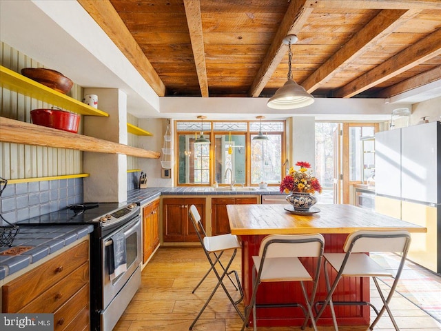 kitchen with light hardwood / wood-style floors, white refrigerator, a kitchen breakfast bar, beam ceiling, and stainless steel electric range oven