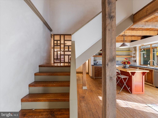 stairway featuring beamed ceiling, wood-type flooring, and sink