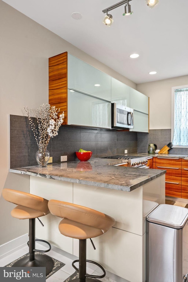 kitchen featuring decorative backsplash, kitchen peninsula, appliances with stainless steel finishes, a kitchen bar, and light tile patterned floors