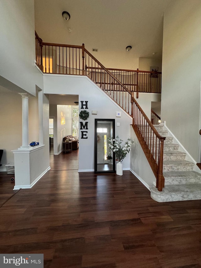 staircase featuring hardwood / wood-style floors, a towering ceiling, and decorative columns