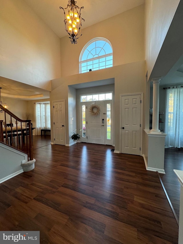 foyer entrance featuring a notable chandelier, dark hardwood / wood-style floors, ornate columns, and a high ceiling