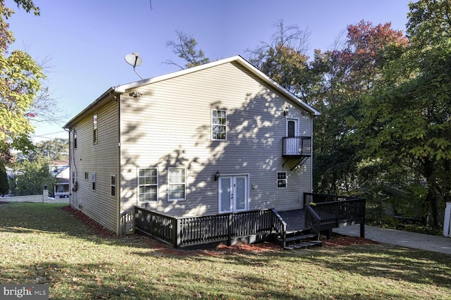 rear view of house featuring a deck, a lawn, and a balcony