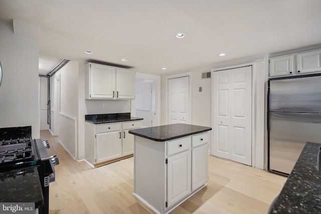 kitchen with gas stove, stainless steel refrigerator, light hardwood / wood-style floors, dark stone counters, and white cabinetry