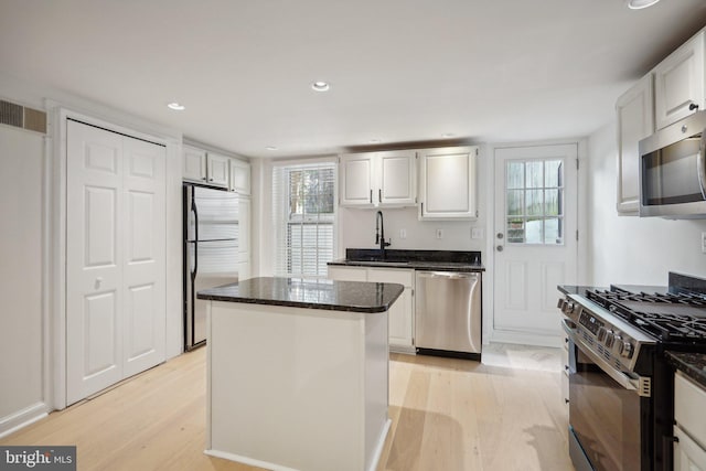 kitchen featuring light wood-type flooring, a center island, white cabinets, sink, and appliances with stainless steel finishes