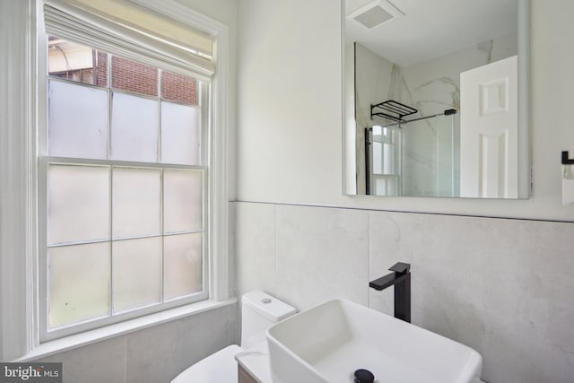 bathroom featuring walk in shower, tile walls, sink, and toilet