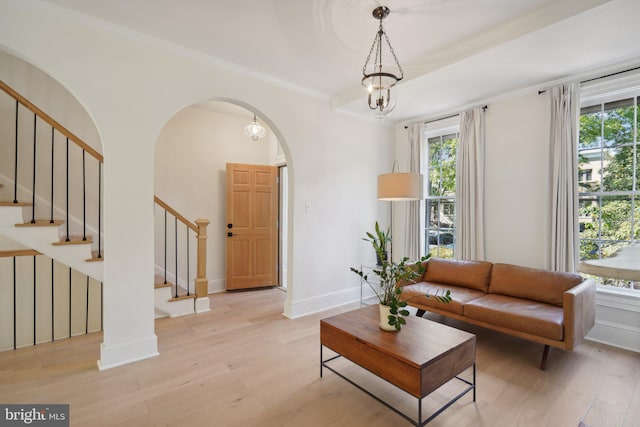 living room featuring plenty of natural light, crown molding, a chandelier, and light wood-type flooring