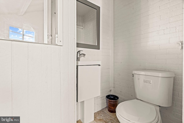 bathroom featuring brick wall and toilet