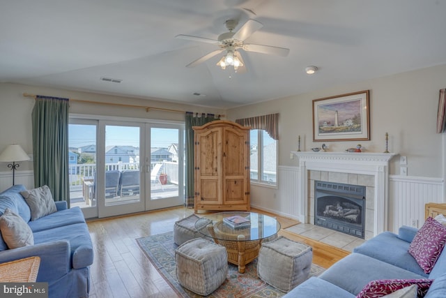 living room featuring ceiling fan, light wood-type flooring, and a tiled fireplace