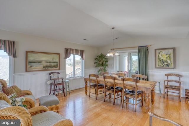 dining area with light wood-type flooring, a notable chandelier, and vaulted ceiling