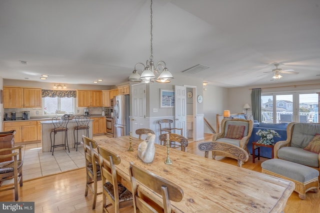 dining area with ceiling fan with notable chandelier, light hardwood / wood-style flooring, and a wealth of natural light